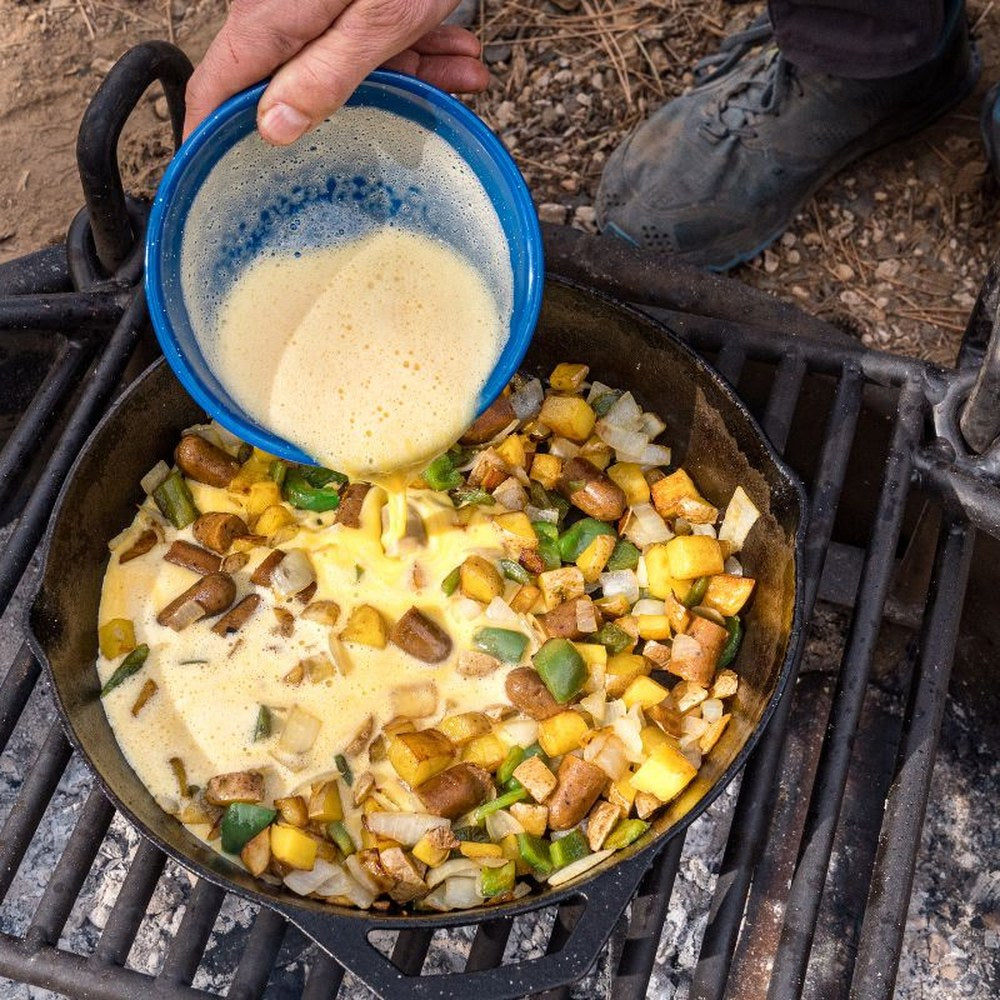 Cast-iron skillet with eggs and potatoes cooking outdoors