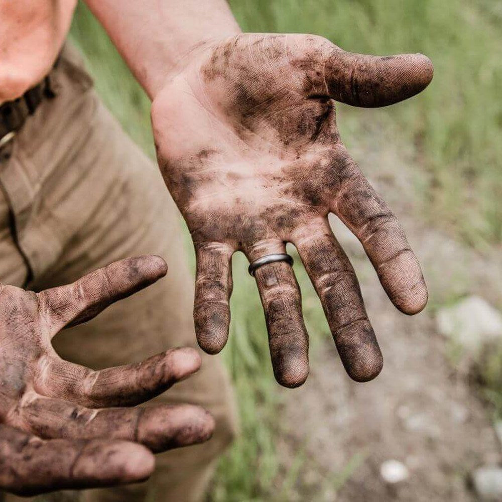 Two open hands covered in dirt and dust held out over grass after a day working outdoors
