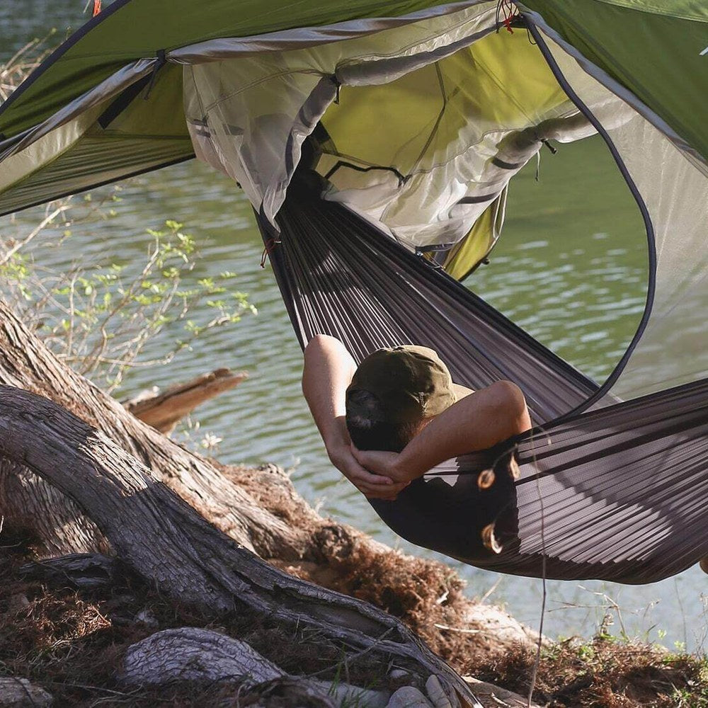 Camper relaxing in the Sunda 2.0 suspended in hammock mode above a creek bank